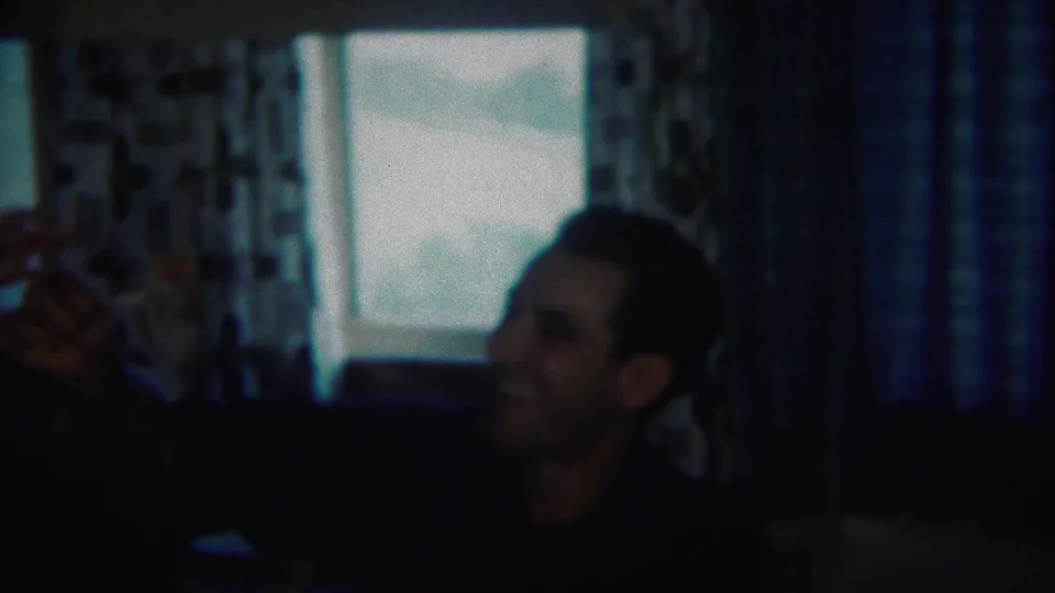 Adult man appears to smile or talk while gesturing in a 1951 Westville family home-movie interior.