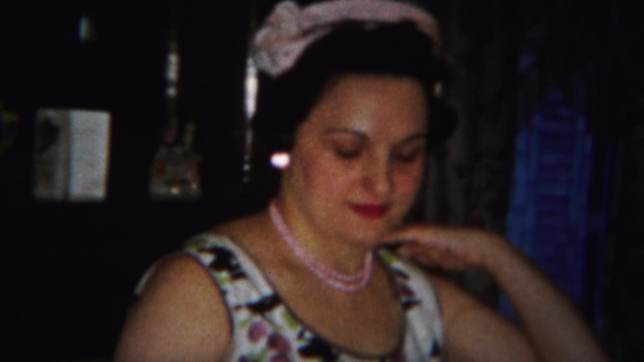 Woman in floral dress and pale headwear looks down in a dim interior.
