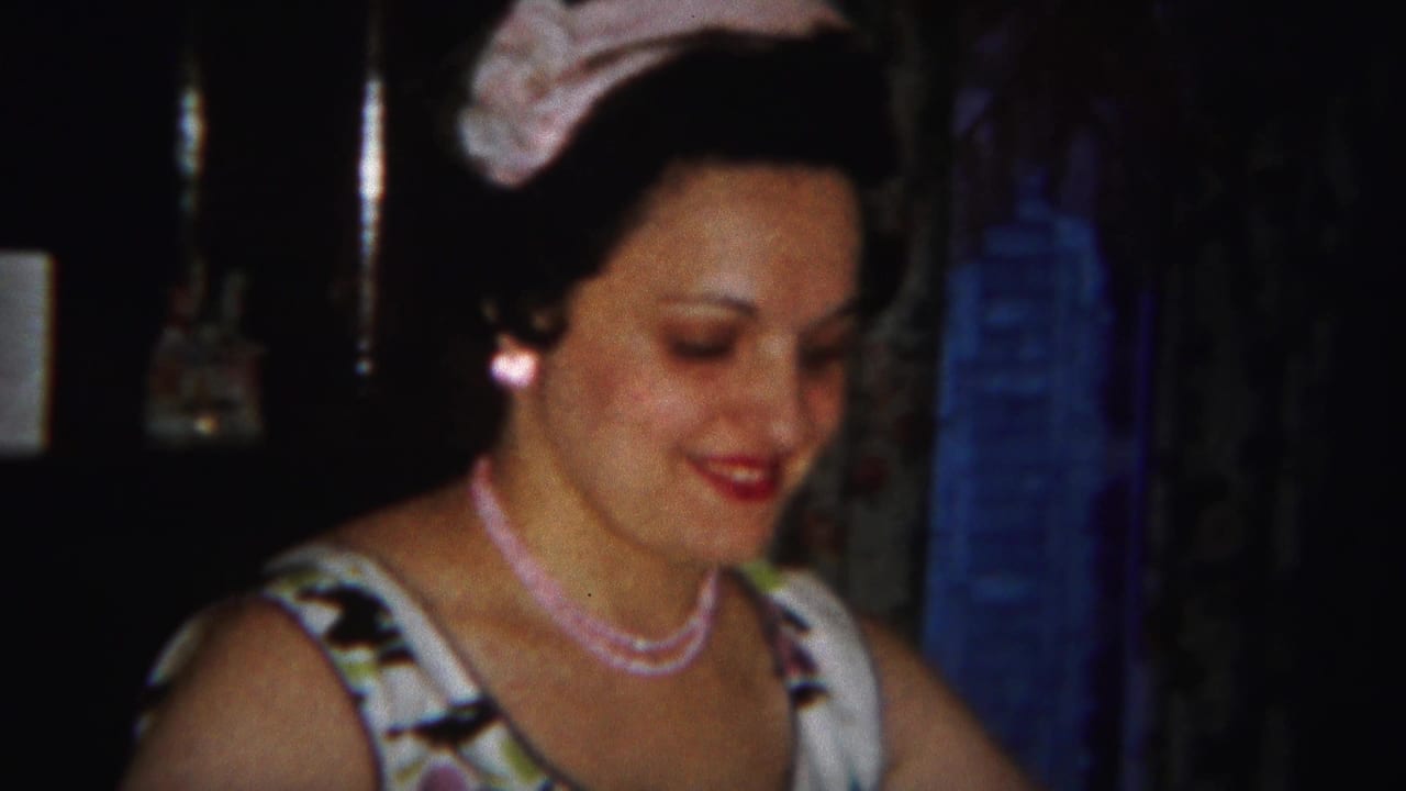 Woman in pale headwear smiles while looking down in a dark room.