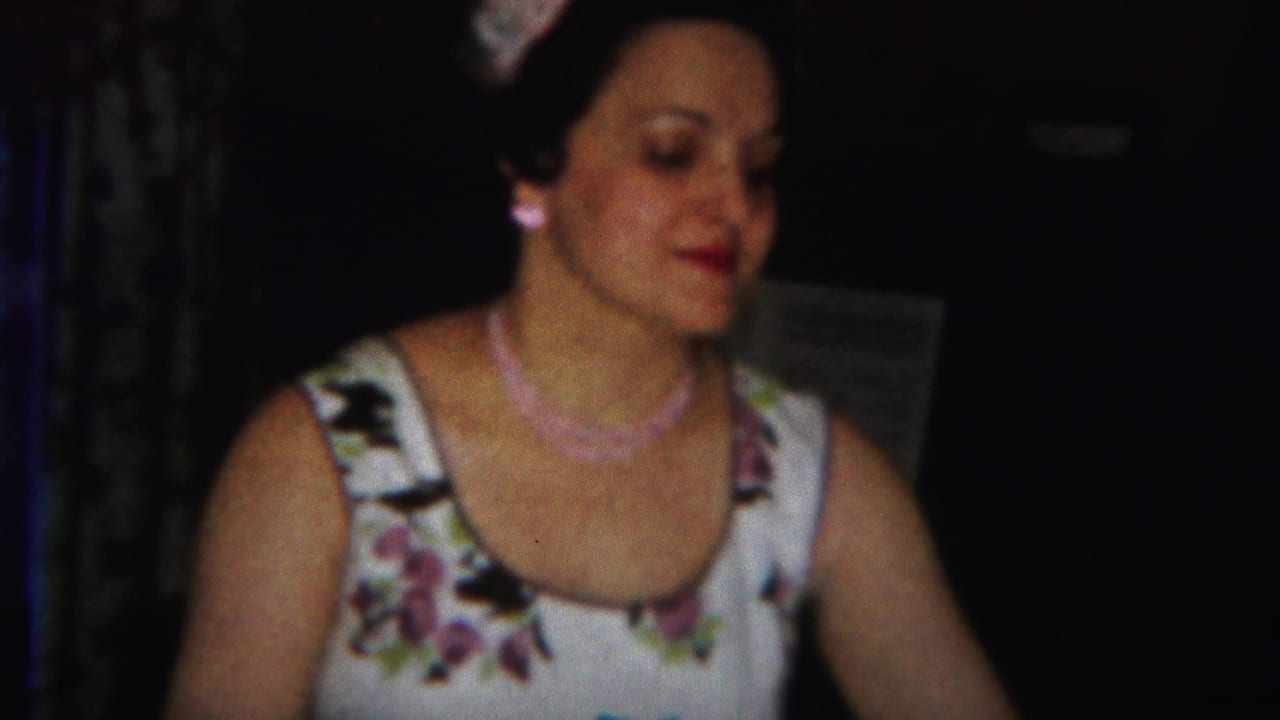 Adult woman in a floral sleeveless dress seated in a dim interior.