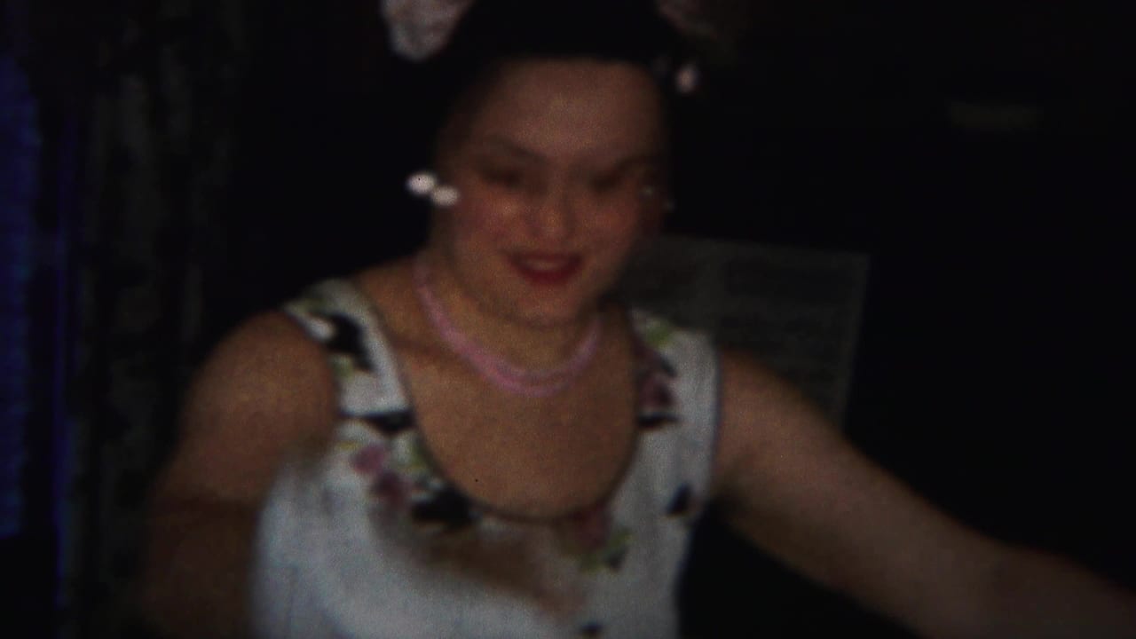 Woman in a floral white dress smiles in a dim indoor room.