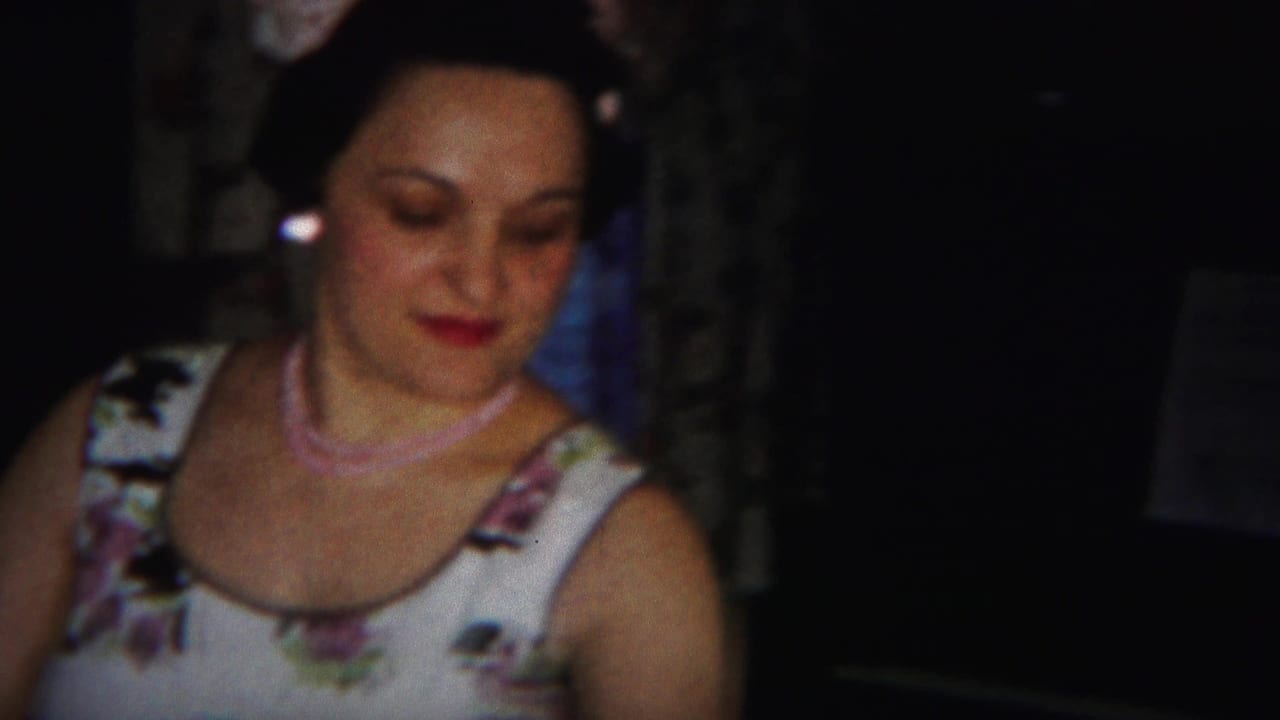 Woman looks downward while wearing a floral dress and pink necklace.