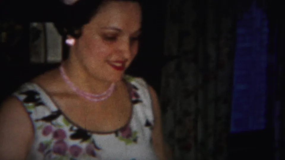 A closer 1951 home-movie view shows the woman smiling softly in a floral white dress inside a private Westville interior.