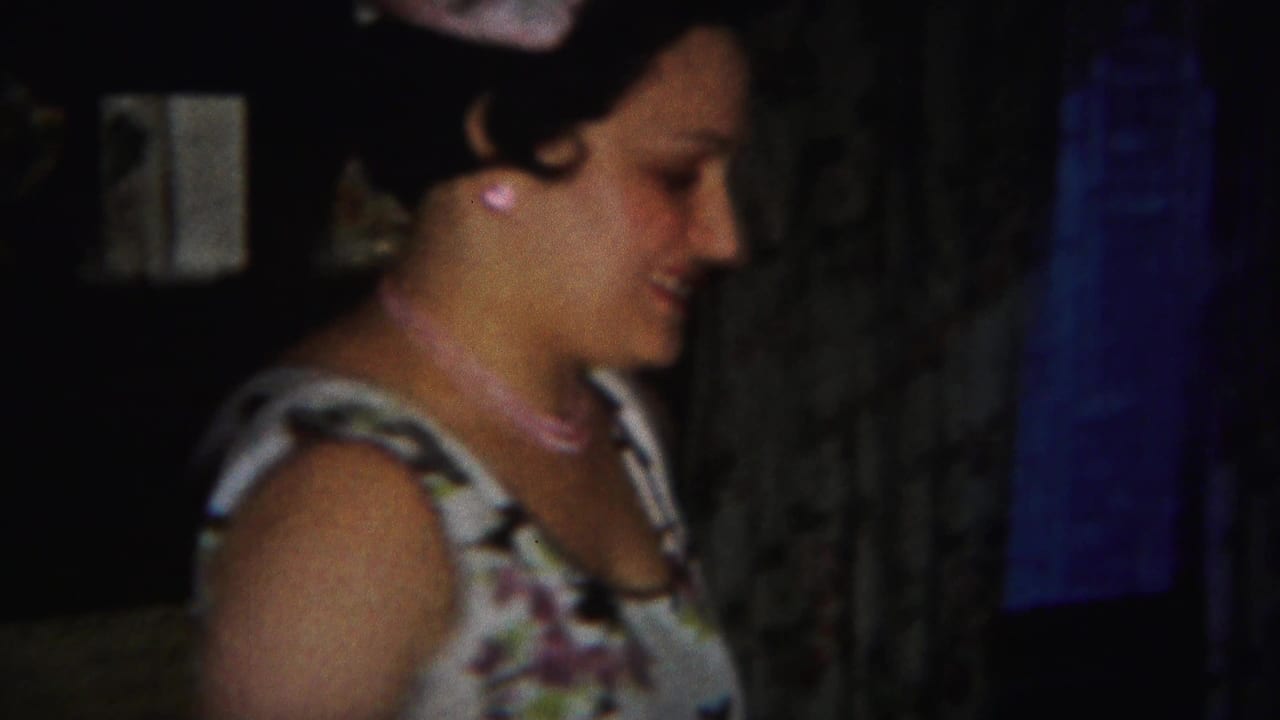 Woman in a floral dress looks down in a dim home interior.