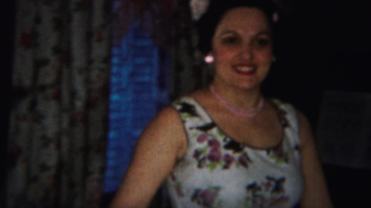 Smiling adult woman in a floral dress appears in a softly focused 1951 home-movie frame inside a Westville residence.
