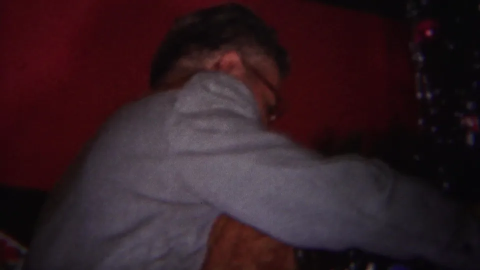 In 1951 Westville home-movie footage, a man in a gray sweater leans close to a decorated Christmas tree in a dim interior.