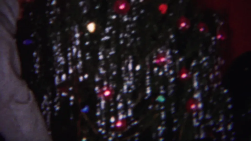 The frame focuses on the Christmas tree, showing dense silver tinsel, colored ornaments, and a partial gray sleeve at the edge.