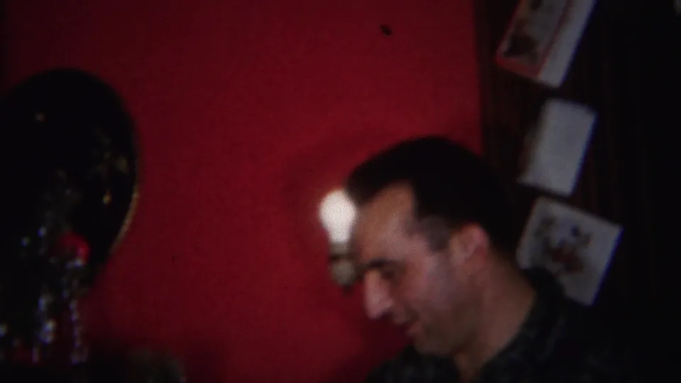 A smiling man appears beside the Christmas tree decorations in the 1951 Westville home interior, with a sconce on the red wall.