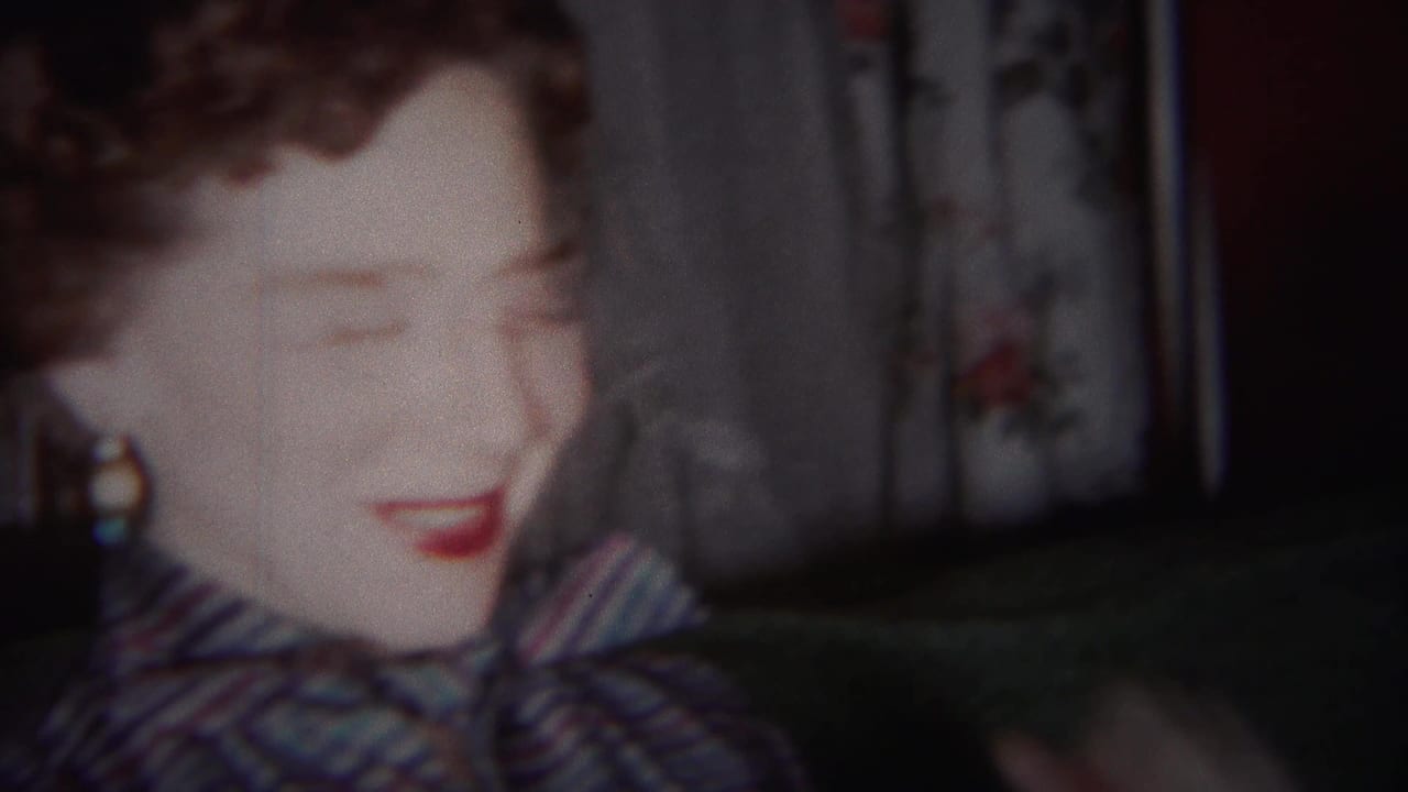Close 1951 Westville frame of the woman laughing in a blue patterned dress, with curtains and a dark interior behind her.