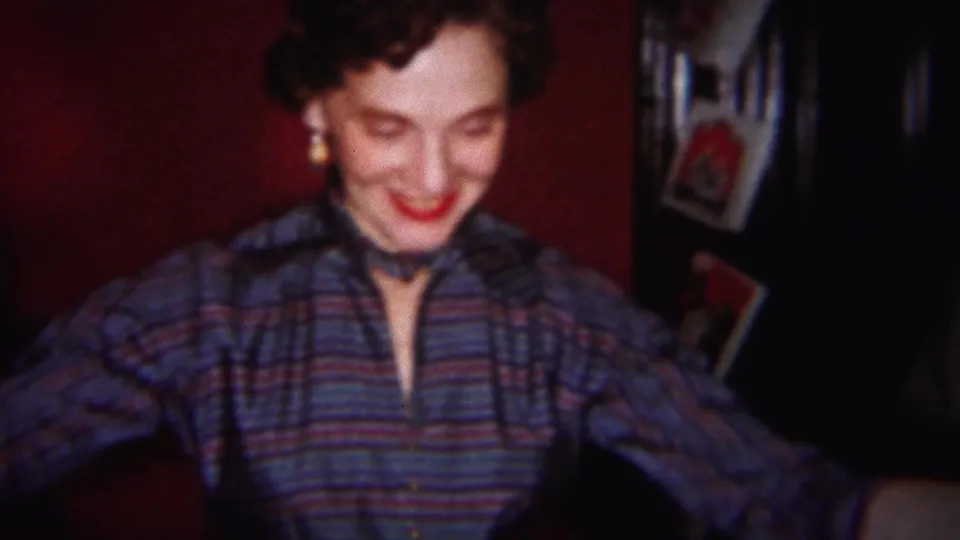 A smiling woman in a striped collared shirt looks down in a softly focused 1951 Westville home-movie frame.