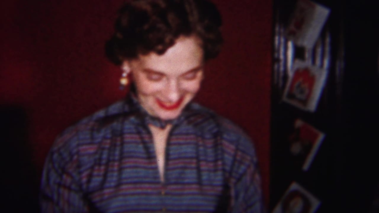 Woman in a striped shirt smiles while looking down in a dim red-walled room.