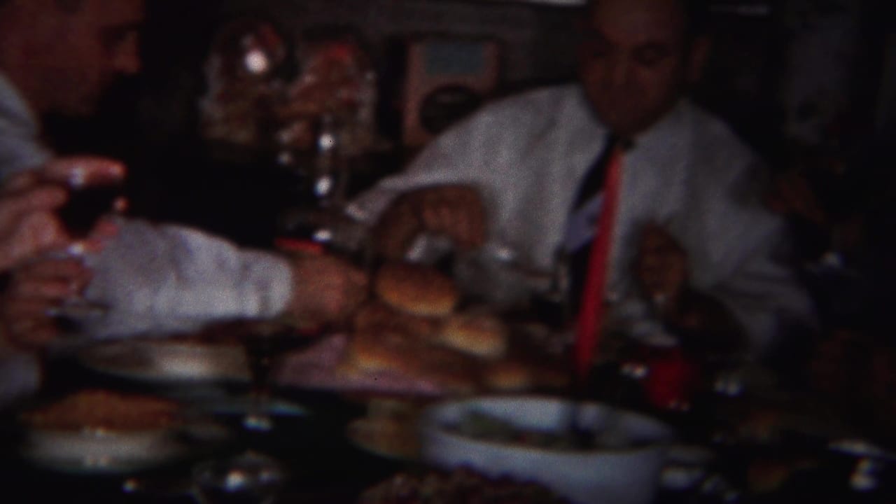 Adults seated around a dim dining table with bread rolls, plates, and wine glasses.