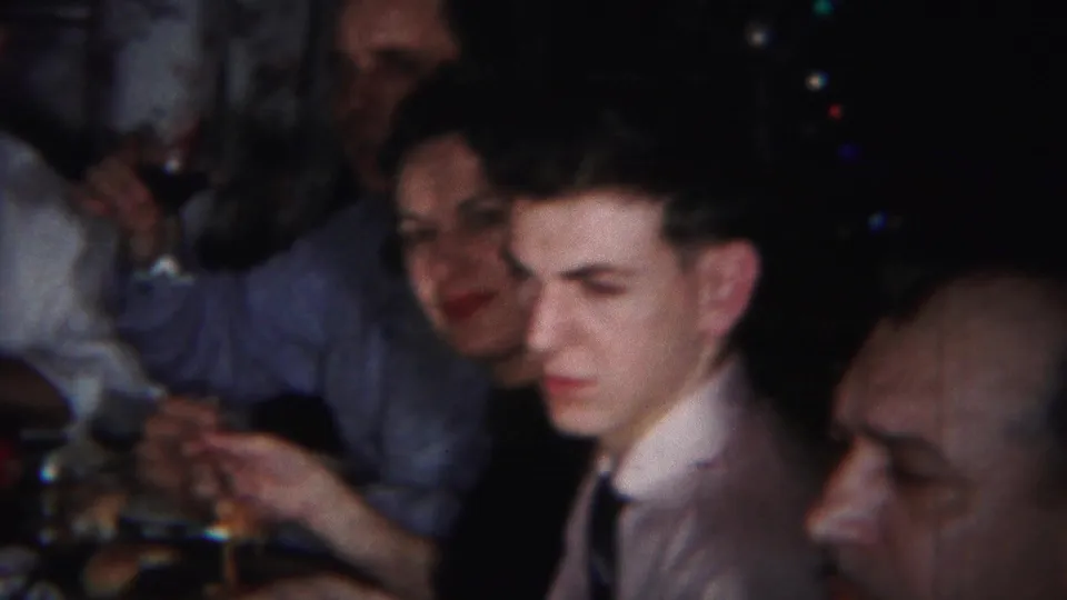 1951 Westville, New Jersey home-movie frame of adults at a family meal, with one person raising a glass and others seated nearby.