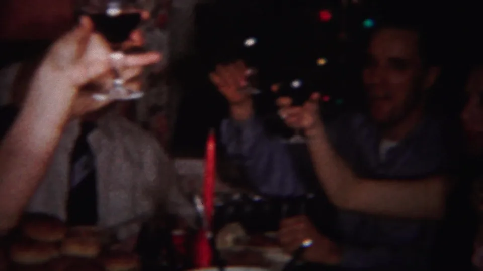 1951 Westville, New Jersey frame showing a close family-table toast with raised glasses, bread rolls, plates, and seated adults.