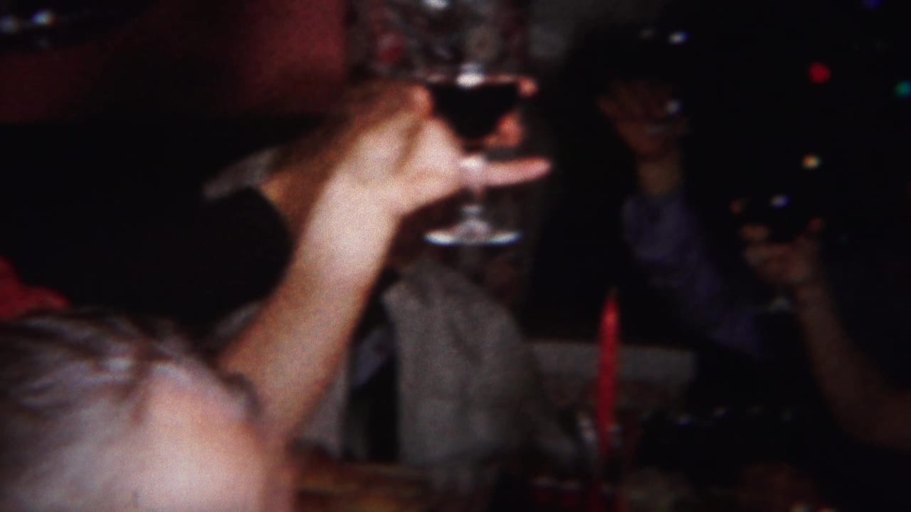 Close interior party view with a raised stemmed glass and adults partly visible in dim light.
