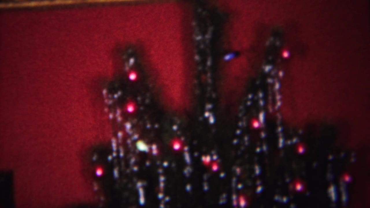Close view of a Christmas tree with tinsel and small colored lights against a red background.