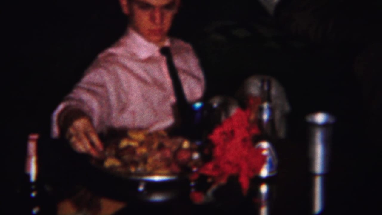Boy in shirt and tie serves a platter at a dim dinner table.