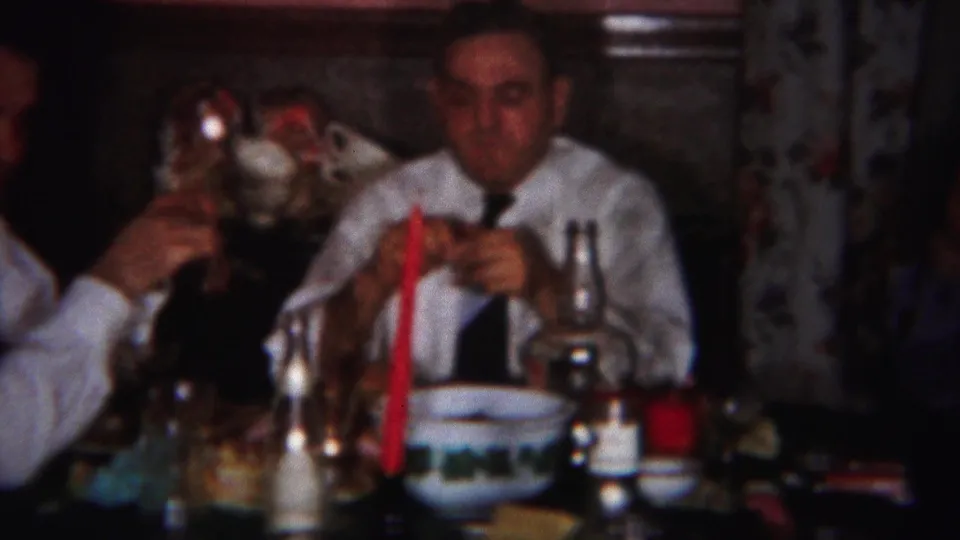 Two men in white shirts and ties sit at a dim dinner table in the 1951 Westville home movie.