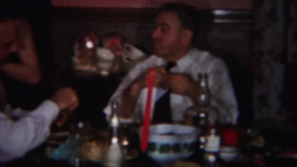 1951 Westville, New Jersey home-movie frame of a man at a dining table with tableware, bottles, and a tall red candle.