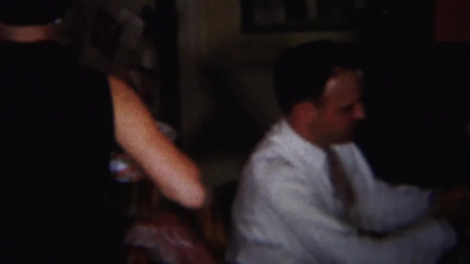 An adult man in a white shirt and tie sits in profile at a dinner table inside the dimly lit Westville holiday gathering.