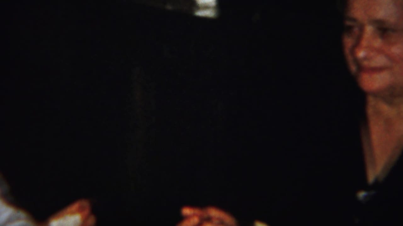 Woman in a dark blouse seated at a dim dinner table, partly cropped by the frame.