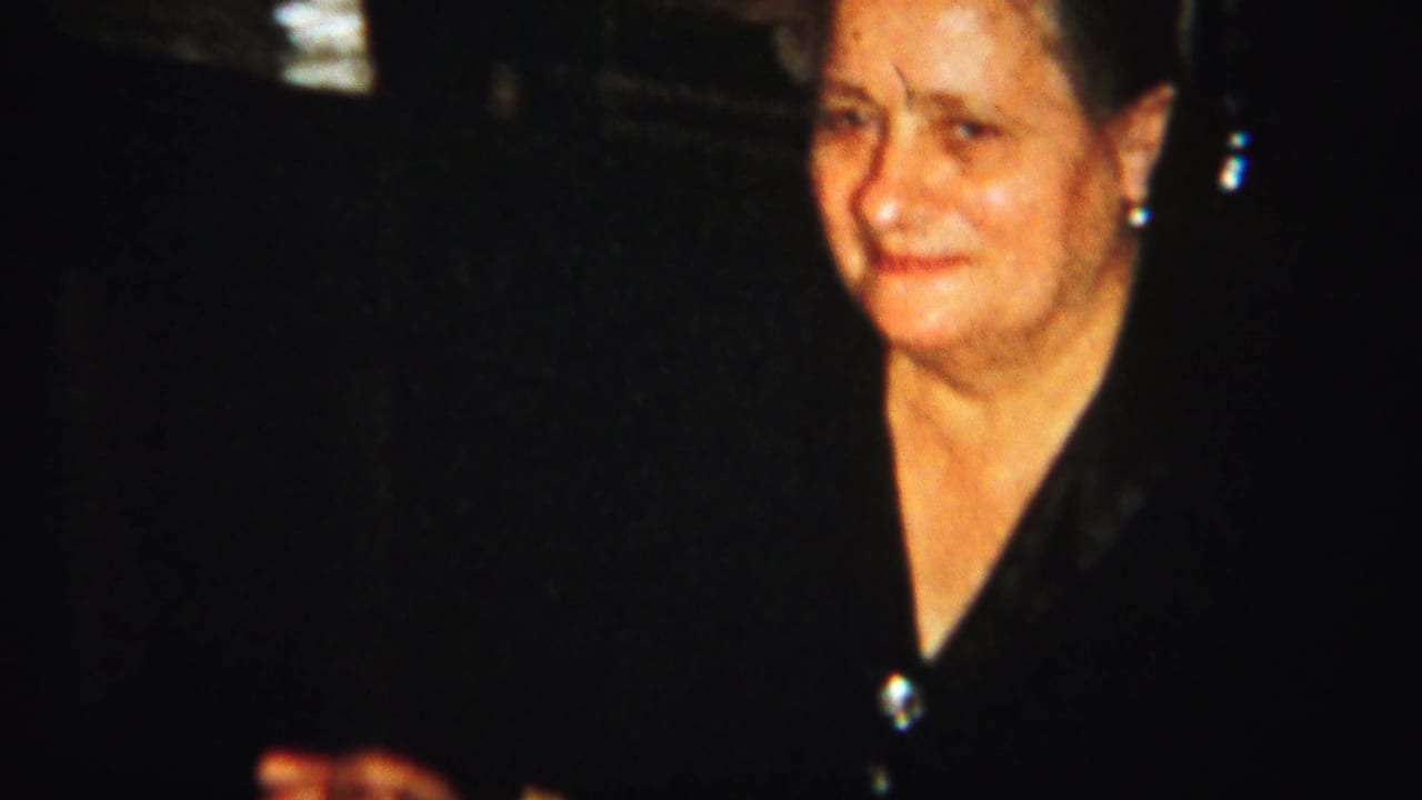 Woman in a dark blouse facing the camera in a dark interior.
