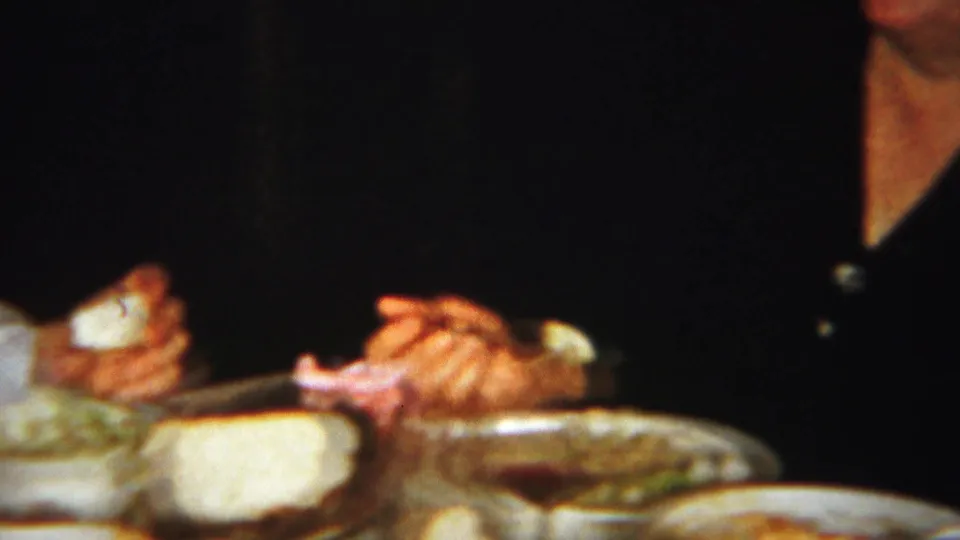 Close 8mm view of hands, utensils, plates of food, and bread during the Westville dinner scene.