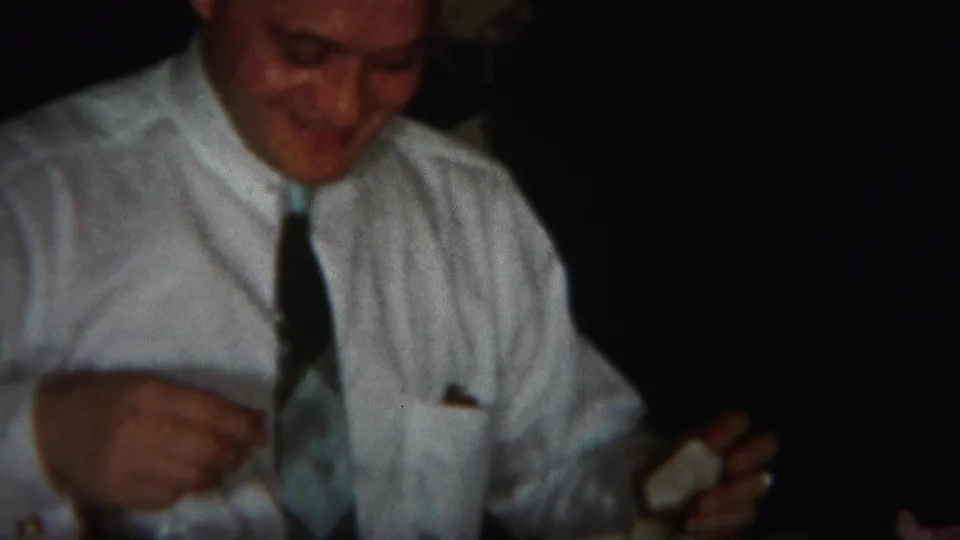 A man in a white shirt and tie eats at the table in the 1951 Westville home-movie dinner footage.