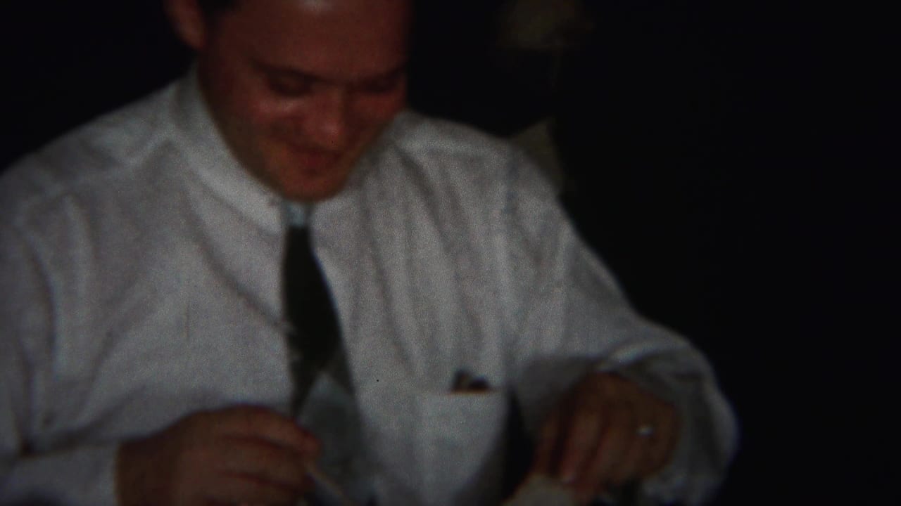 Man in a white dress shirt and tie smiles while seated at a dark table.