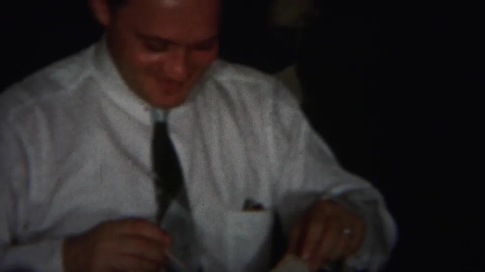 In 1951 Westville, New Jersey home-movie footage, a man in a white shirt and tie smiles as his hands rest near a table setting.