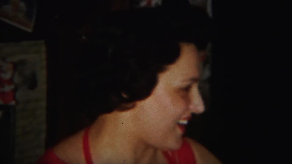 A smiling woman in a red dress is seen in profile in the Westville, New Jersey 1951 home-movie dining scene.