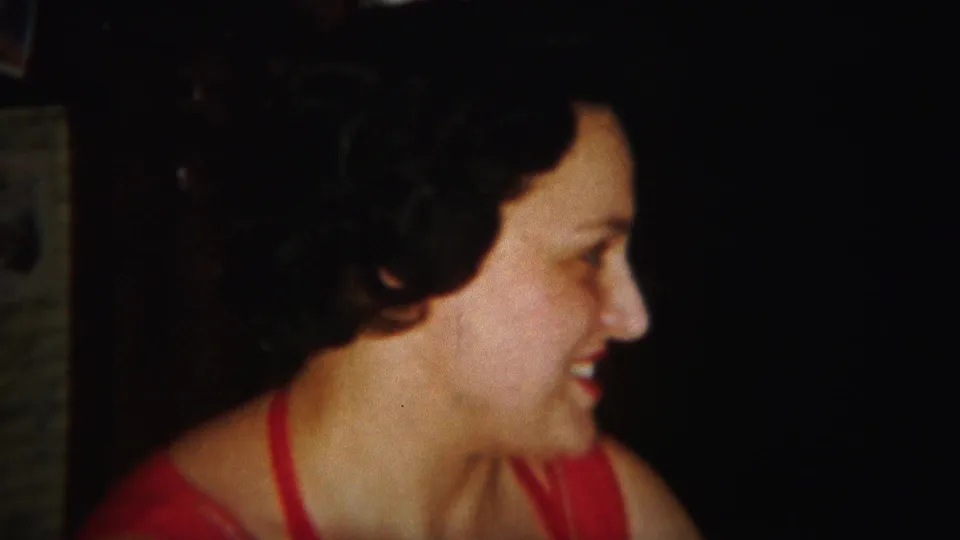 The woman in the red dress remains in profile, smiling toward someone off frame in the 1951 Westville home-movie clip.