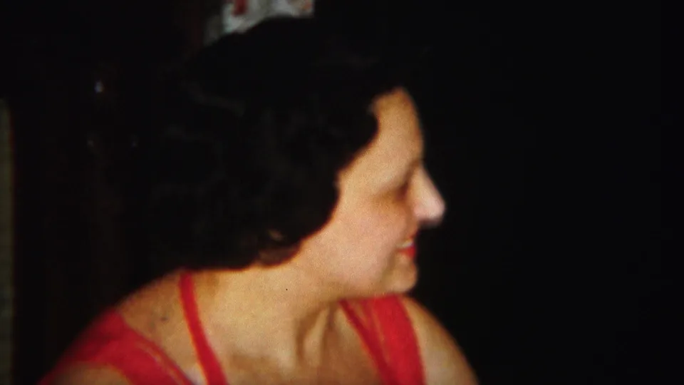 The close-up continues as the woman faces right, her dark hair and red dress visible against a dim background.