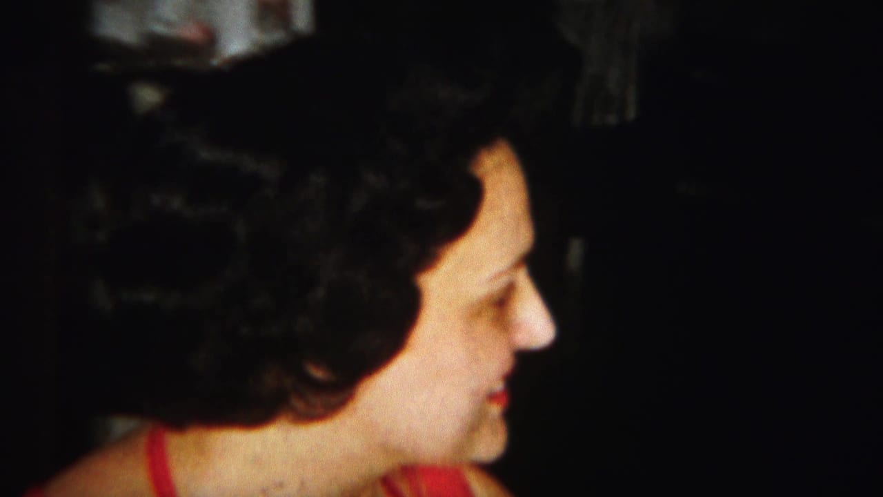 Woman with dark curled hair smiles in profile in a dim indoor setting.