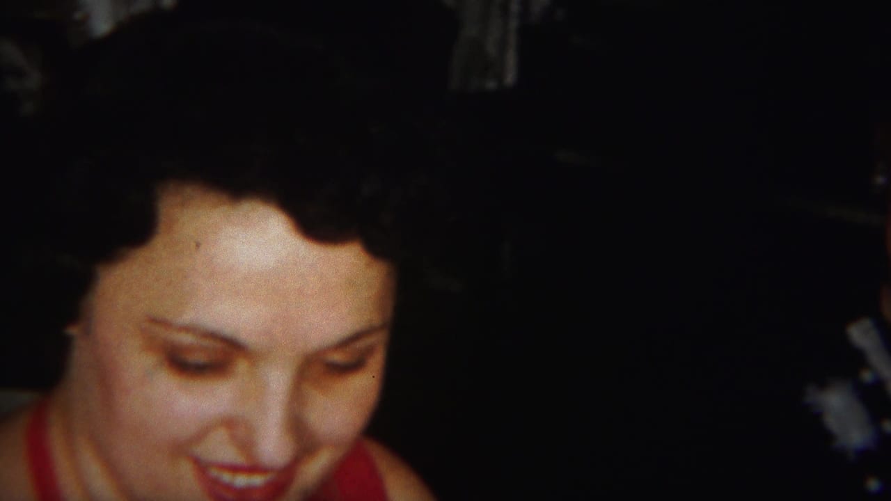Woman with dark hair looks down and smiles in a dim interior.