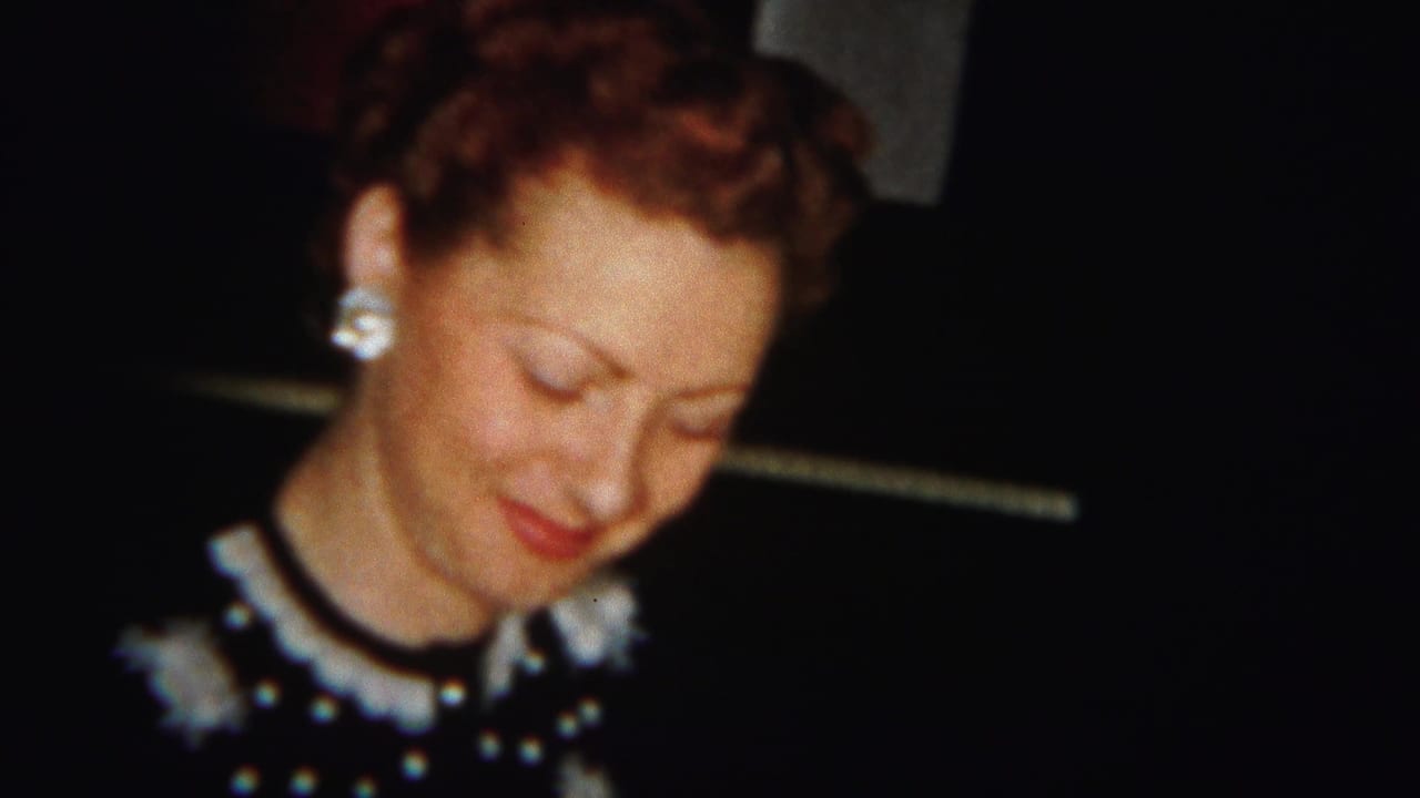 In 1951 Westville home-movie footage, a woman in a dark dress with a white collar and pearl earrings looks down with a soft smile.