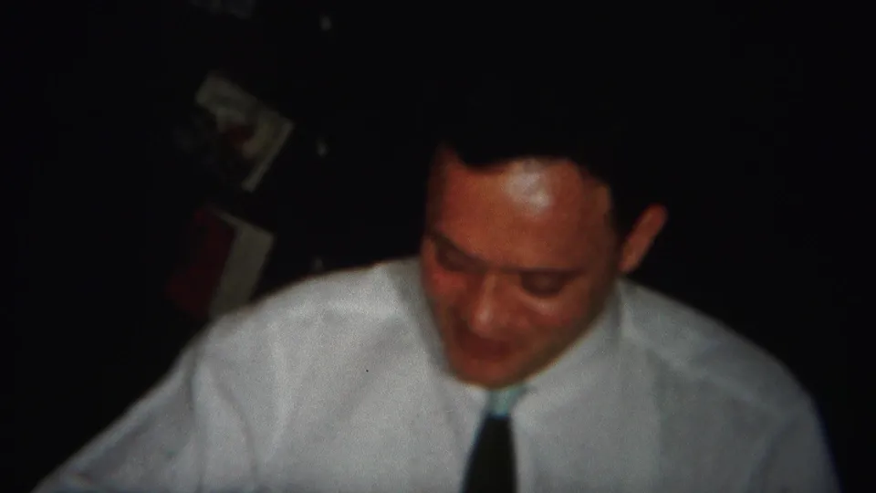 The 1951 home-movie frame shows the man looking down in close framing, with his white shirt and dark tie most visible.