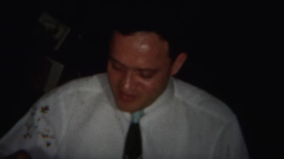 A later frame from the 1951 Westville dinner clip shows the man looking down, with dim light and a dark tabletop or foreground edge.
