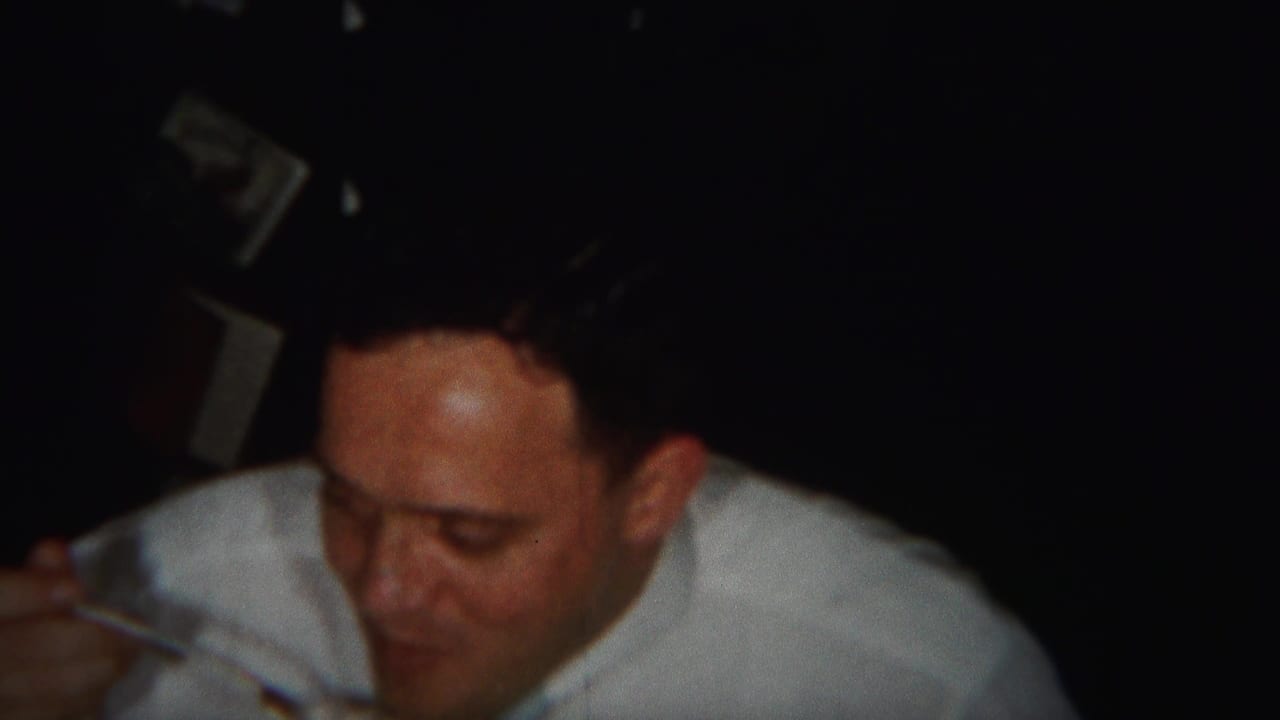 Man in a white shirt chews while holding a fork near his mouth.