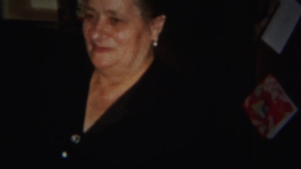 An older woman, likely the mother described in the clip metadata, looks on with a soft expression in the Westville home setting.