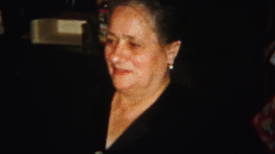 The older woman remains framed in warm, low light, wearing a dark top and earrings in the 1951 Westville family interior.
