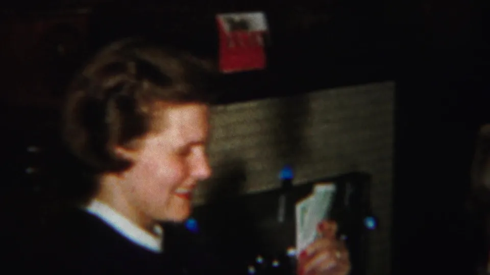 A woman with curled hair smiles over a hand of cards in this warm 1951 Westville home-movie frame.