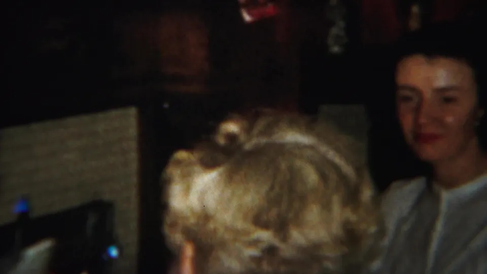 A blonde-haired adult is seen from behind while a dark-haired woman faces the camera in a 1951 Westville interior.