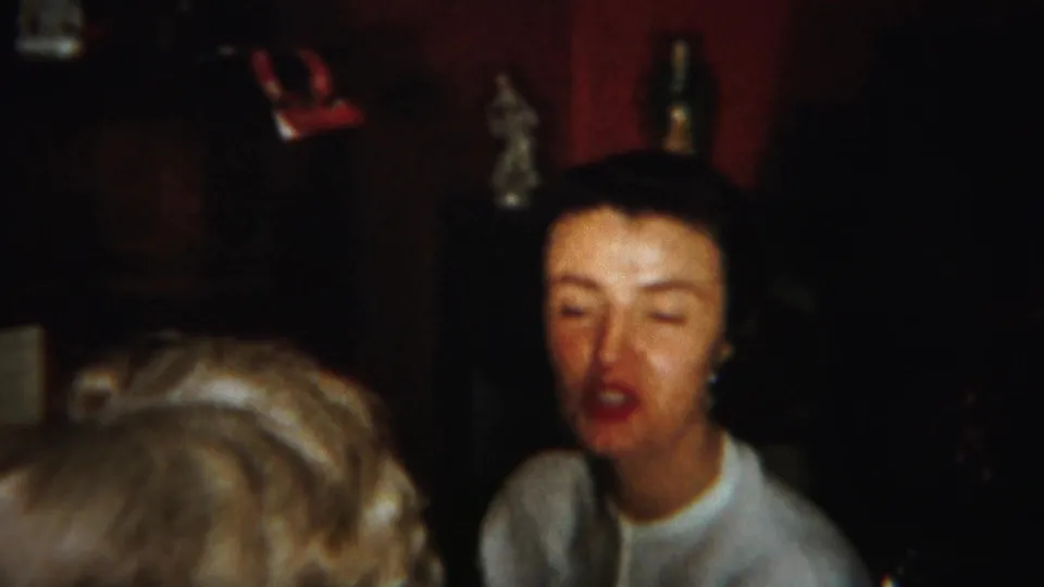 A dark-haired woman appears mid-conversation behind a blonde-haired adult in a warm 1951 Westville home interior.