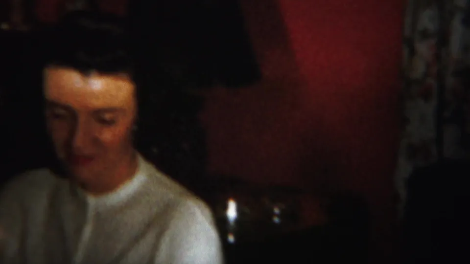 A softly focused home-movie frame shows a woman seated near the edge of a Westville, New Jersey interior gathering.