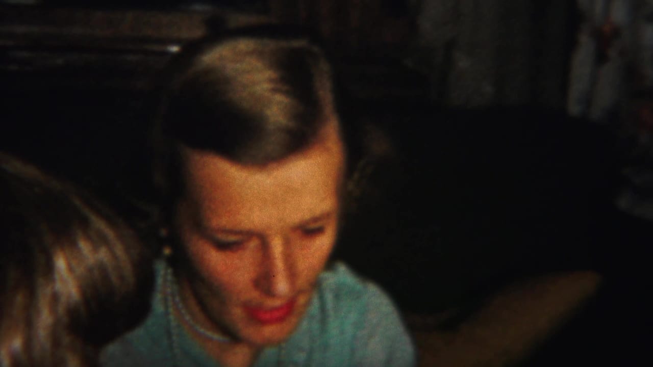 Adult woman in a light blue top and pearl necklace looks down in a dim Westville, New Jersey interior, with another head in the foreground.