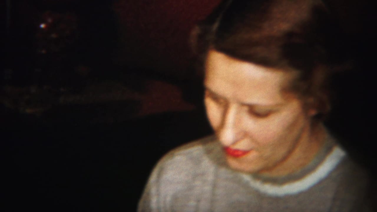 Woman in a gray sweater looks downward against a dark background.