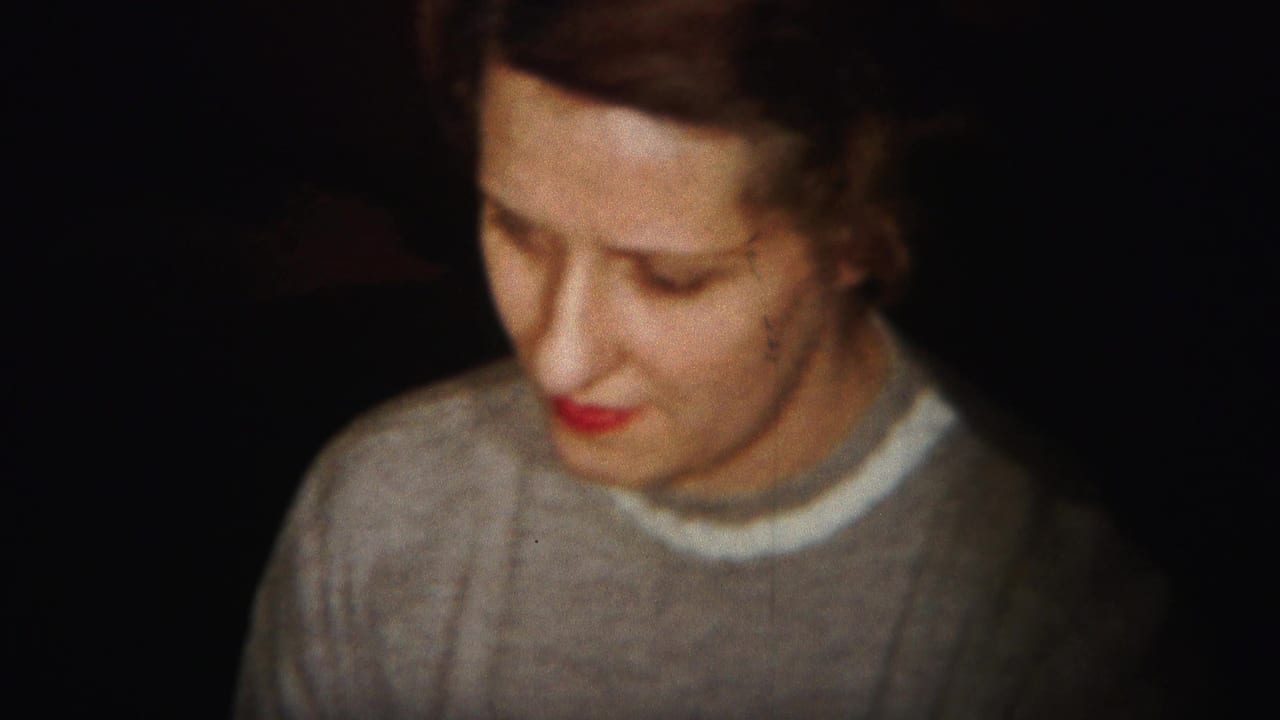 Woman in a gray sweater looks down in a dim interior.