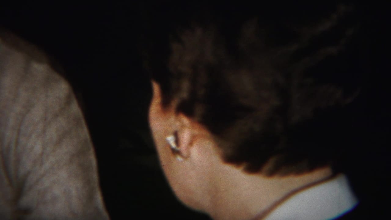 Woman seen from behind beside another partially visible adult in a dark interior.