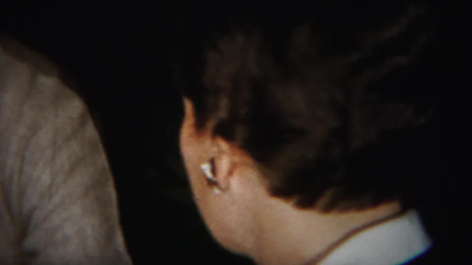 In a 1951 Westville, New Jersey home movie, a woman is seen from behind during an indoor gathering with another adult partly visible.